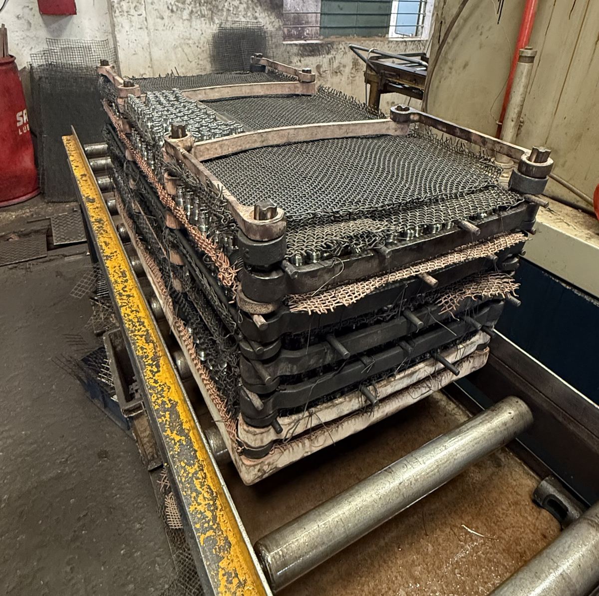 Stacked mesh fixture trays on the roller conveyor that feeds the furnace line.