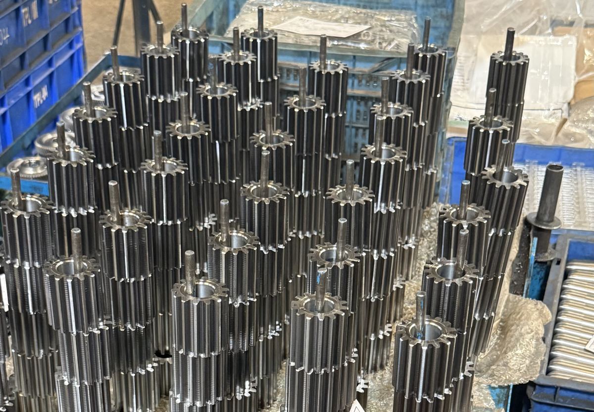 Rows of splined gear shafts standing upright in a fixture on the STEP shop floor.